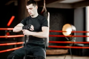 Boxer wrapping hand with black sports bandage before training in a boxing ring